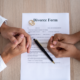 Hands clasped together over a divorce form with wedding rings and a pen.