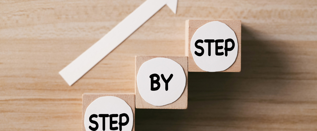 Three wooden blocks labeled “Step by Step” stacked upward with a white arrow pointing forward.