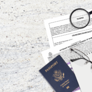 Documents for name change and a U.S. passport on a desk with glasses, pen, and magnifying glass