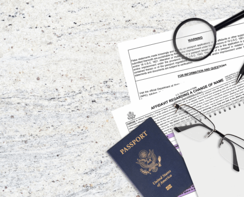 Documents for name change and a U.S. passport on a desk with glasses, pen, and magnifying glass